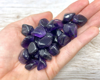 A hand holding a selection of A grade Amethyst tumbled crystals 
