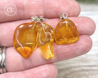 A hand holding three Baltic Amber Mini Pendants with silver tone findings