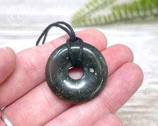 A hand holding a Bloodstone donut necklace on a black cord 