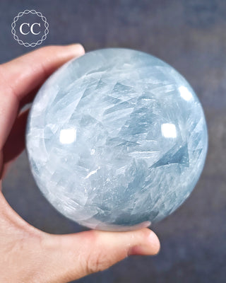 A hand holding a Blue Calcite sphere from Madagascar