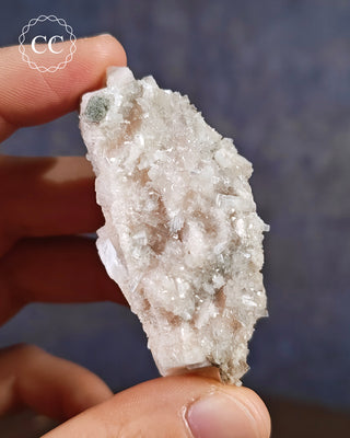 Brewsterite on Calcite from Scotland, in hand on blue background