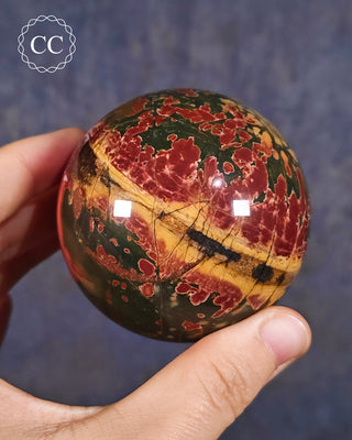 A hand holding a Cherry Creek Jasper Sphere