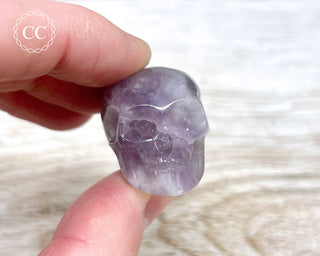 Fingers holding a Chevron Amethyst crystal skull carving