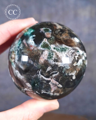A hand holding a Cosmic Jasper Sphere from Madagascar