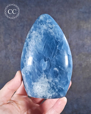 A hand holding a deep Blue Calcite freeform from Madagascar