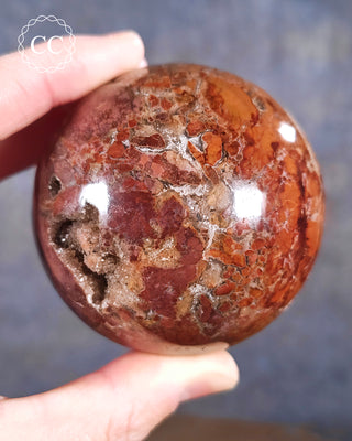 A hand holding a Druzy Brecciated Jasper Sphere from Madagascar