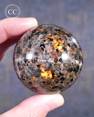 A hand holding a polished UV reactive Syenite fluorescent Sodalite sphere, also known as Firestone, Emberlite or Yooperlite