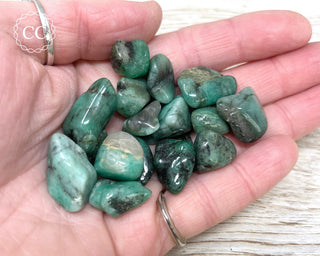 A hand holding a selection of Emerald tumbled crystals 
