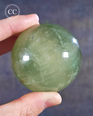 A hand holding a Green Fluorite Sphere from Madagascar