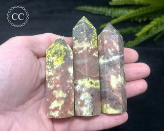A hand holding three Green Opal and Red Calcite towers