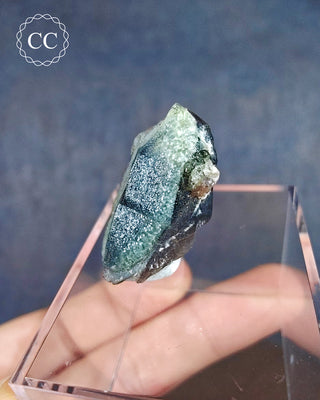A Hyalite Opal on a dark Smoky Quartz point from Namibia displayed on a clear box