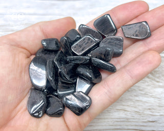 A hand holding a selection of small Hypersthene tumbled crystals 
