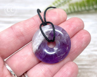 A hand holding an Amethyst donut pendant with a black cord 