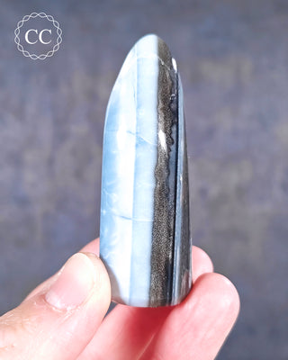 A hand holding a banded Blue Opal Freeform from Rajasthan, India
