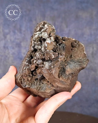 A hand holding a specimen of Siderite and Calcite that displays an iridescence