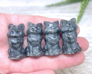 A hand holding 4 Larvikite Fox carvings