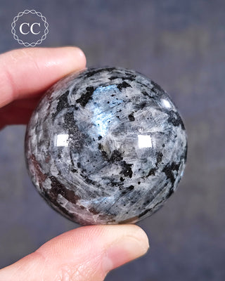 A hand holding a Larvikite sphere from India