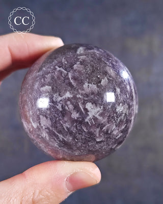 A hand holding a Lepidolite sphere from Madagascar