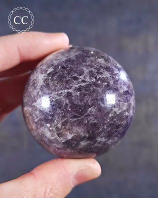 A hand holding a Lepidolite sphere from Madagascar