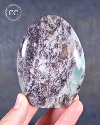 A hand holding a Lepidolite and Cleavelandite freeform from Madagascar