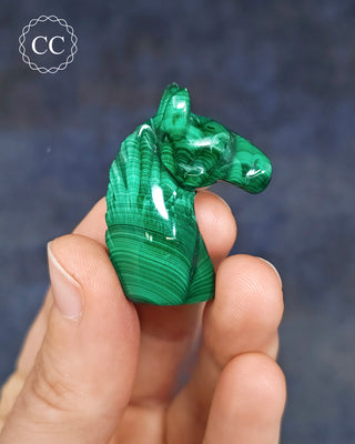 Malachite horse carving in hand on blue background
