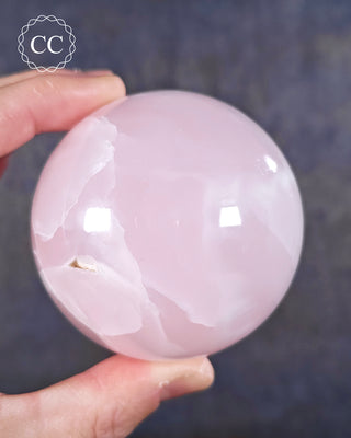 A hand holding a Mangano Calcite Sphere