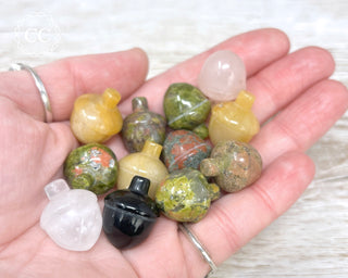 A hand holding 12 mini crystal Acorn carvings in various crystal types 