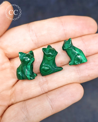 Malachite cat carvings on hand on blue background
