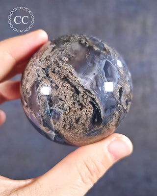 A hand holding a Moss Agate Sphere
