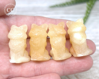 A hand holding 4 Orange Calcite Fox carvings