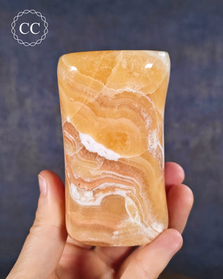A hand holding an Orange Calcite freeform from Pakistan