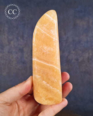 A hand holding an Orange Calcite freeform from Pakistan