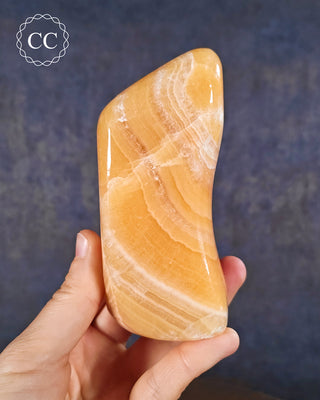 A hand holding an Orange Calcite freeform from Pakistan