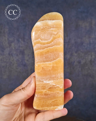 A hand holding an Orange Calcite freeform from Pakistan
