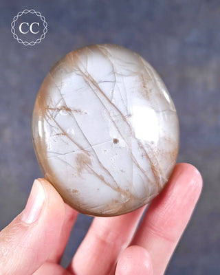 A hand holding a Peach Moonstone palmstone from Madagascar