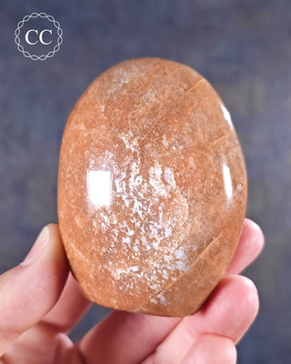 A hand holding a Peach Moonstone freeform from Madagascar with a silvery shimmer