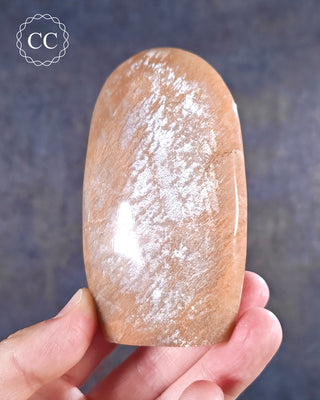 A hand holding a Peach Moonstone freeform from Madagascar with a silvery shimmer