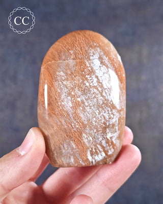 A hand holding a Peach Moonstone freeform from Madagascar with a silvery shimmer