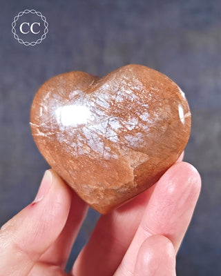 A hand holding a Peach Moonstone Heart from Madagascar