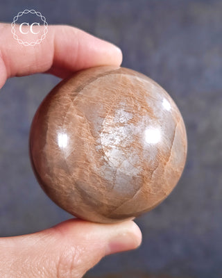 A hand holding a Peach Moonstone sphere from Madagascar