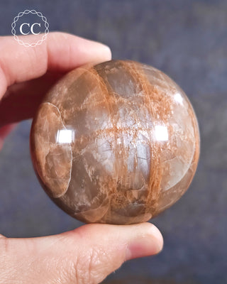 A hand holding a Peach Moonstone sphere from Madagascar