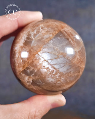 A hand holding a Peach Moonstone sphere from Madagascar