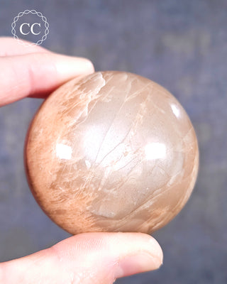A hand holding a Peach Moonstone Sphere from Madagascar 
