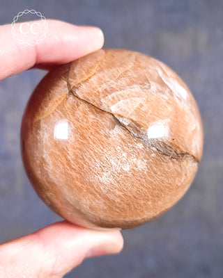 A hand holding a Peach Moonstone sphere from Madagascar 