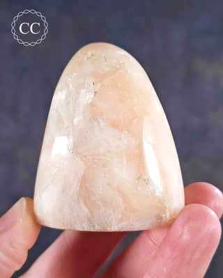 A hand holding a Peach Stilbite Freeform from India 