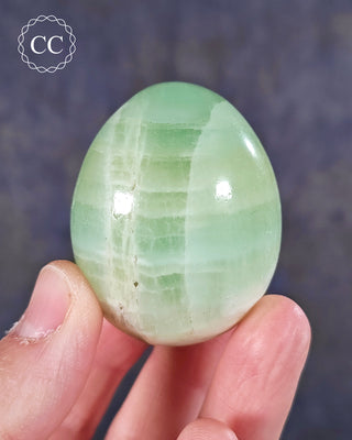 A hand holding a Pistachio Calcite Egg from Pakistan 