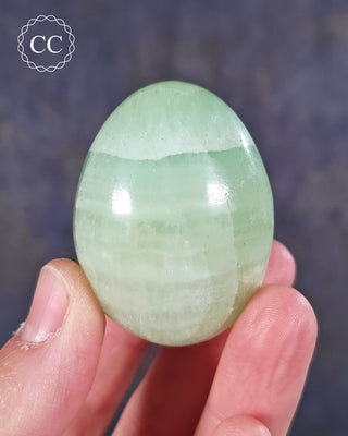 A hand holding a Pistachio Calcite Egg from Pakistan 