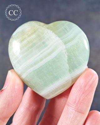 A hand holding a Pistachio Calcite Heart from Pakistan