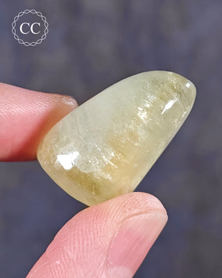 A hand holding a polished Green Apophyllite crystal