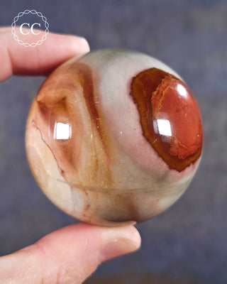 A hand holding a Polychrome Jasper Sphere from Madagascar